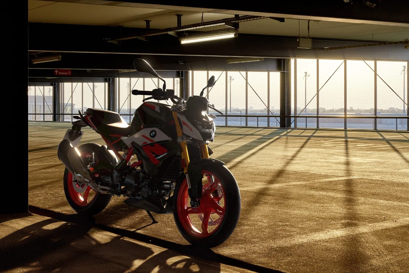 BMW G 310 R com rodas vermelhas em estacionamento com luz de fim de tarde